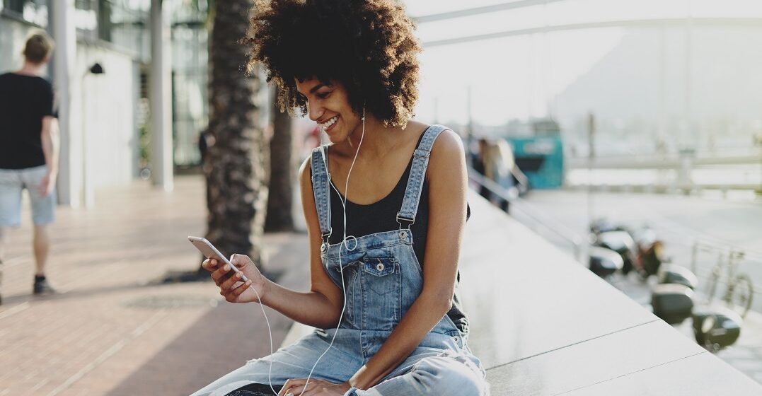 Beautiful girl with headphones on listening to the 10 best bands from France sitting on a wall by the seaside.