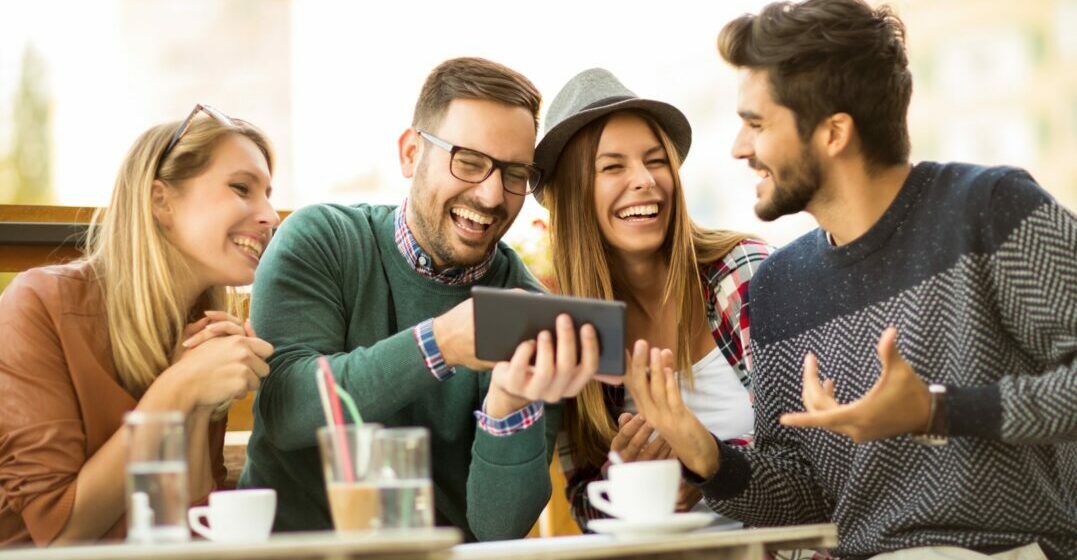 Four friends at a table with an iPad laughing about funny English words
