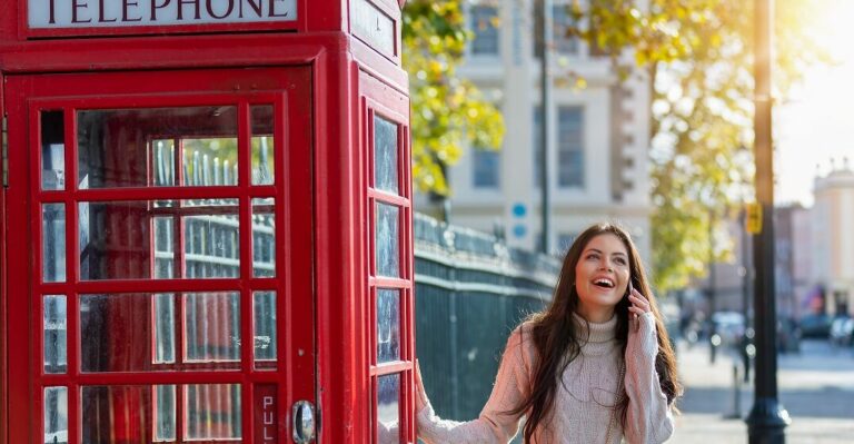 girl next to a typical British phone cabin speaking on her mobile using typical British phrases