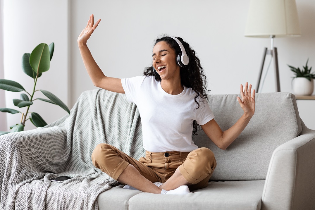 girl with headphones on a sofa singing songs to learn Spanish