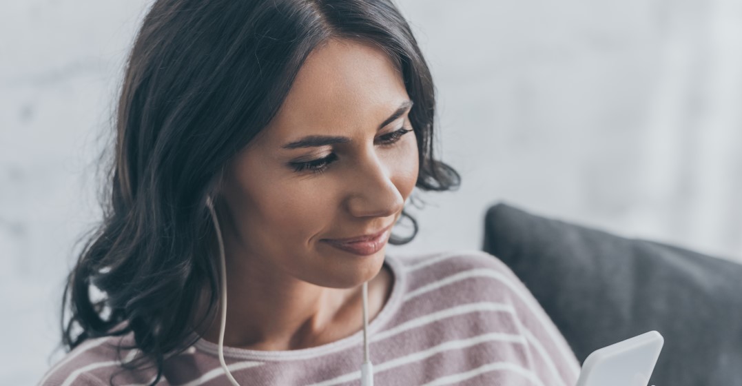 Una mujer con cabello castaño y una camisa gris a rayas tiene auriculares en los oídos mientras aprende sobre el significado de 