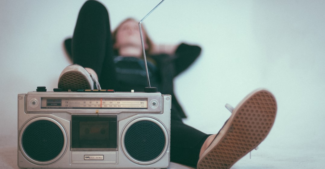 Person hinter einem Radio liegend und französische Bands hört