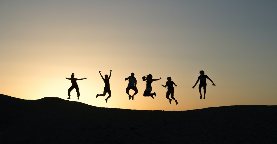 Deutsche Ausdrücke: Freunde springen auf einer Wiese bei Sonnenuntergang