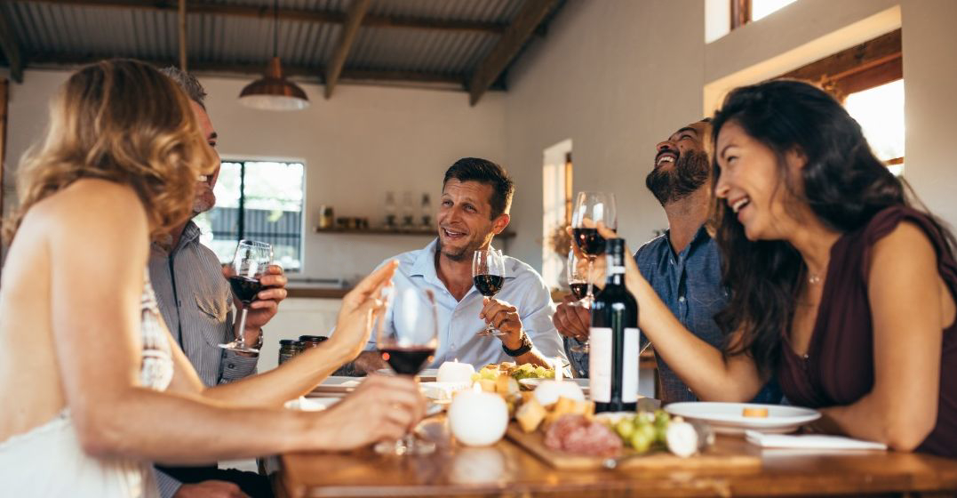 Los amigos se sientan alrededor de una mesa, comiendo y bebiendo vino. Discuten algunas expresiones populares en español.