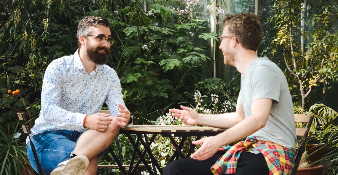 Two men sitting at a garden table exchanging English tautology examples