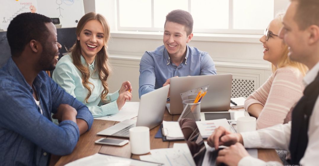 4 Kollegen sitzen an einem Tisch an ihren Laptops und lernen Business-Deutsch