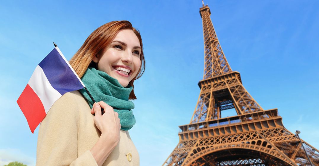 Eine lächelnde Frau unter dem Eiffelturm möchte ihr Französisch verbessern