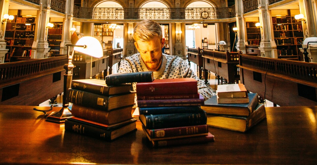 Man in a library with a pile of books studying the differences between dative and accusative in German