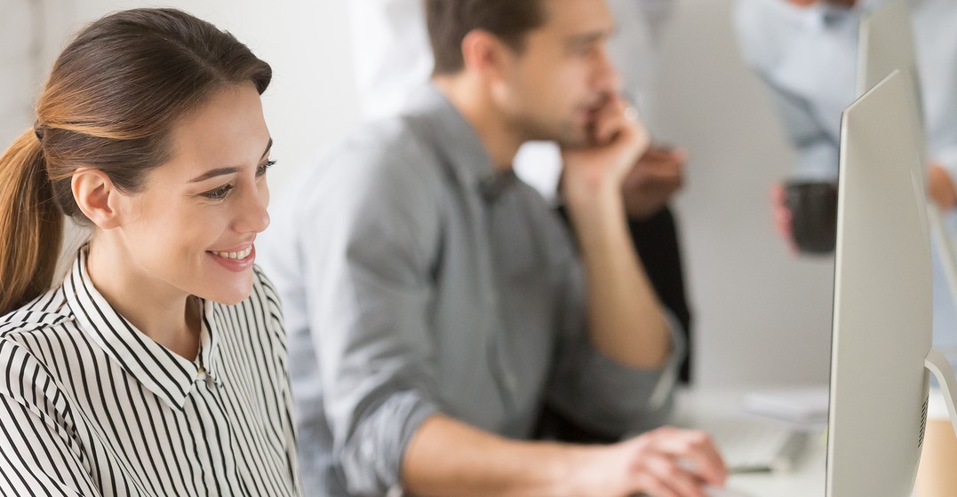 SMiling woman in front of a computer, man in the background researching about the importance of punctuation in English