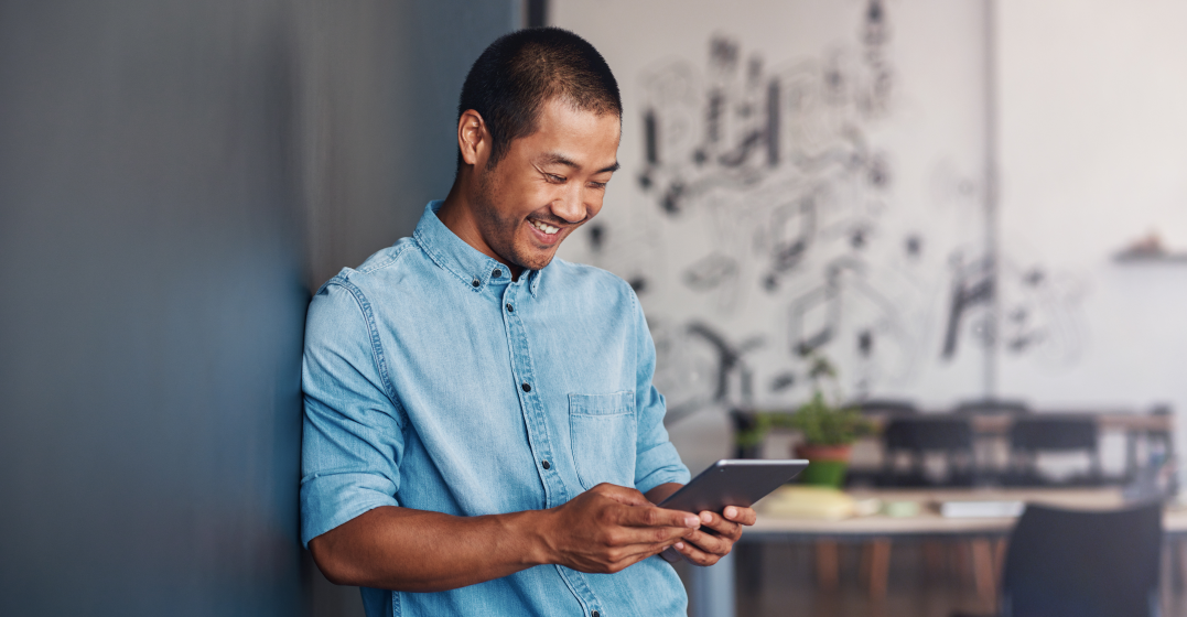man smiling and looking at his tablet as he learns the most common German verbs