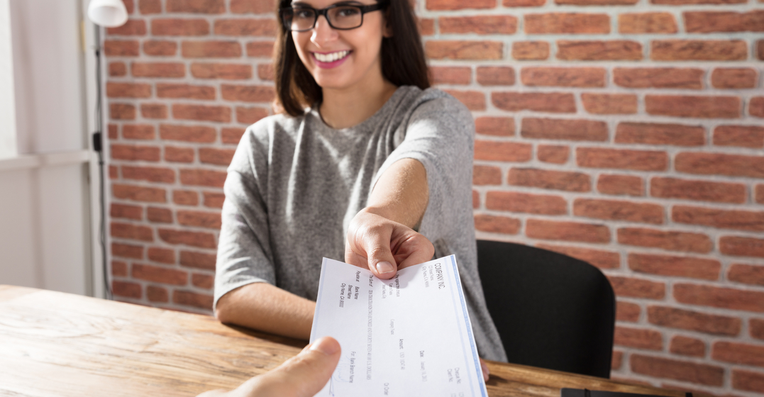 Woman sitting at a table smiling and handing over a cheque