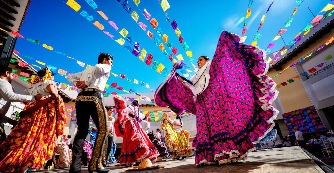 A man and a woman in traditional Mexican dresses dancing in a decorated street
