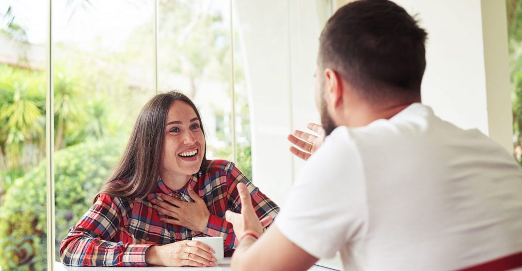 A man and a woman sitting at a table, having a cheerful conversation.