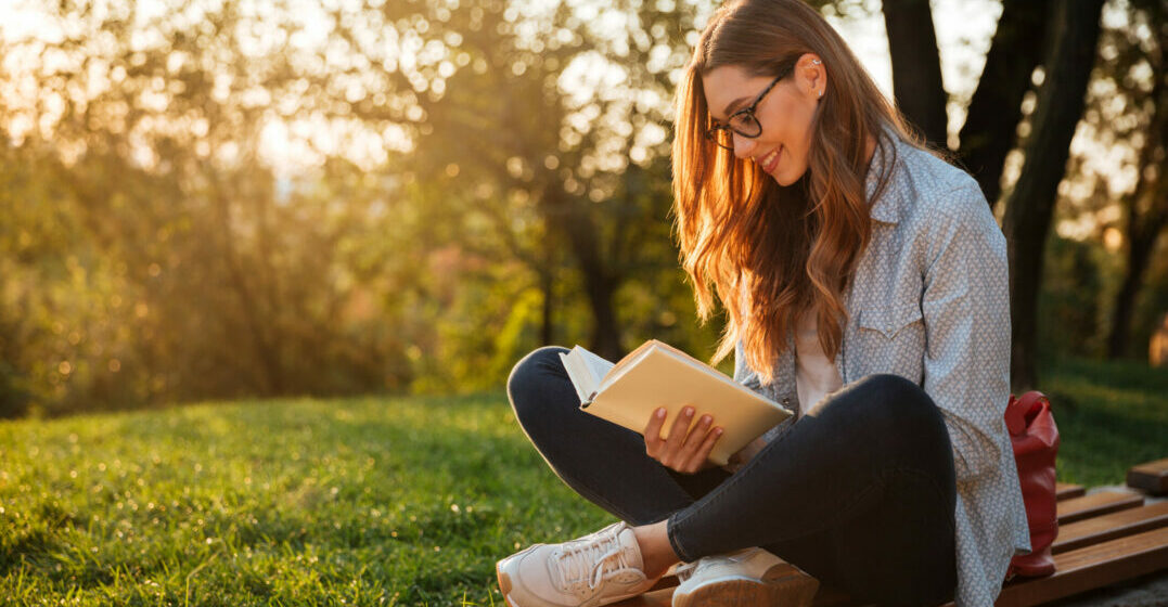 Young woman sitting on a bench outside, reading a book