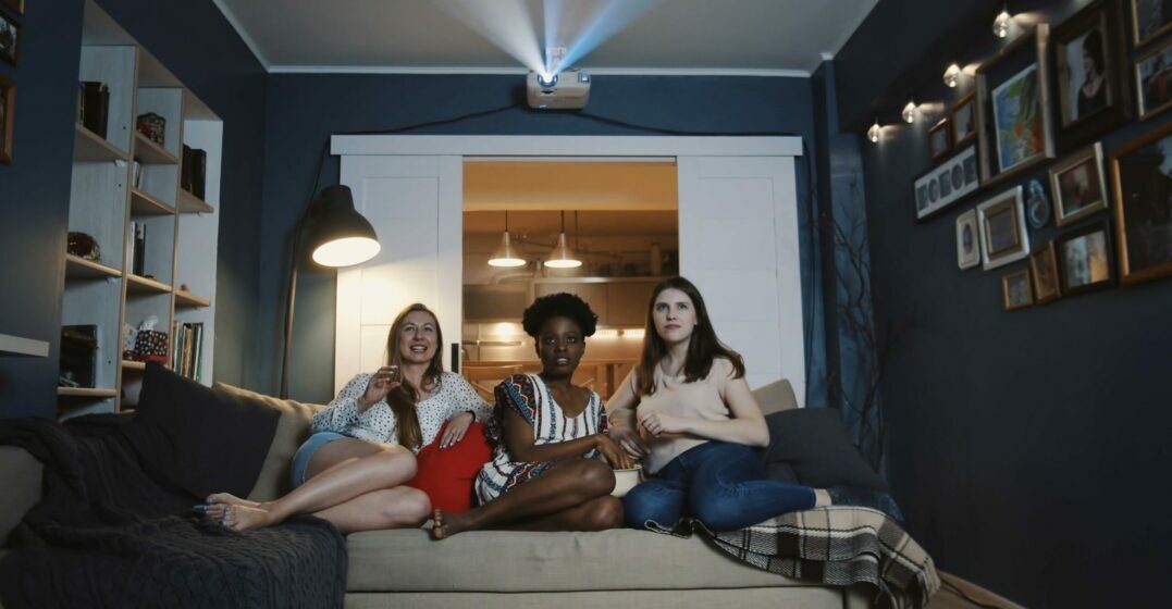 Three friends sitting on a couch watching TV