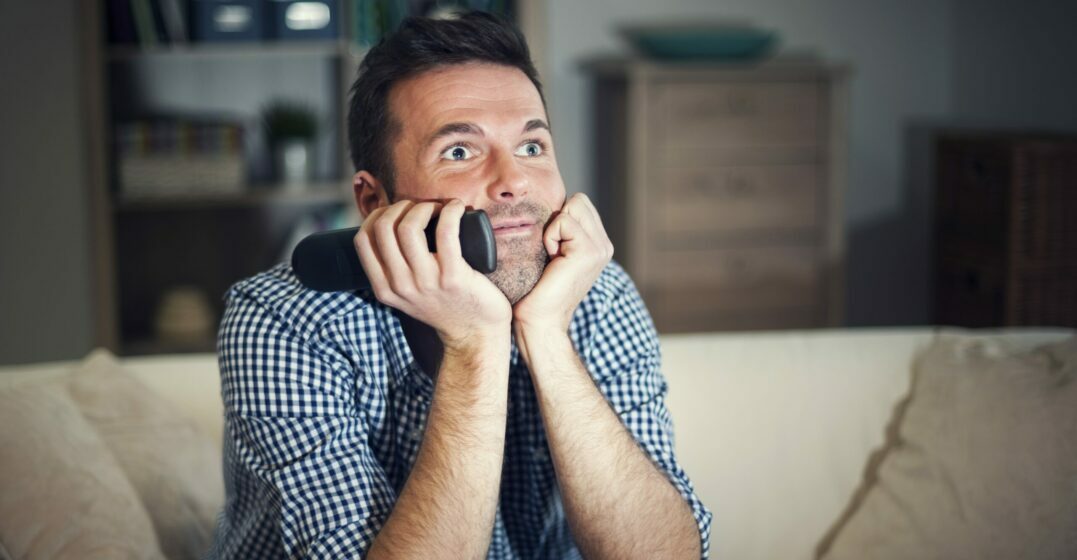 Mann sitzt auf der Couch und lernt mit Serien Englisch