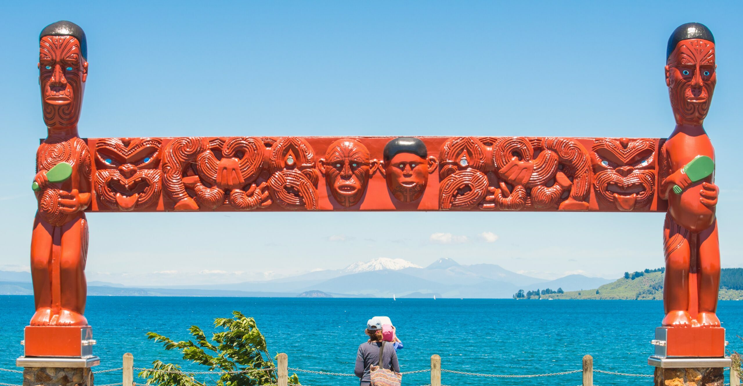 Woman with her baby sitting under the traditional Maori wood carving wondering about New Zealand's languages