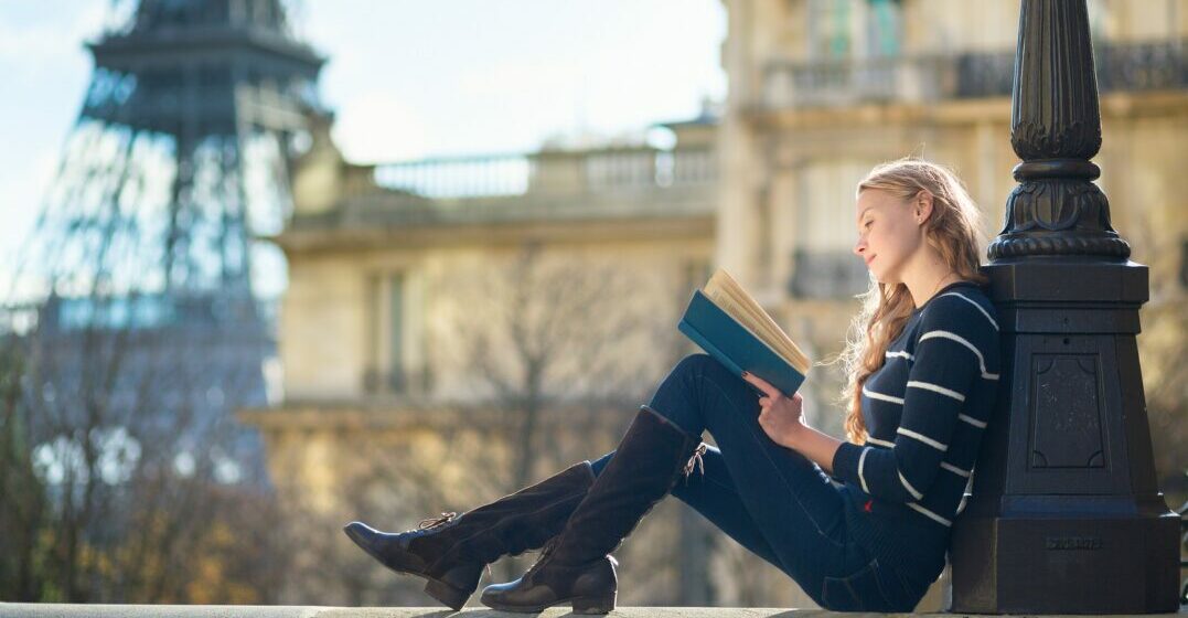 Woman sitting in front of the Eiffel tower reading a book from one of the best French writers