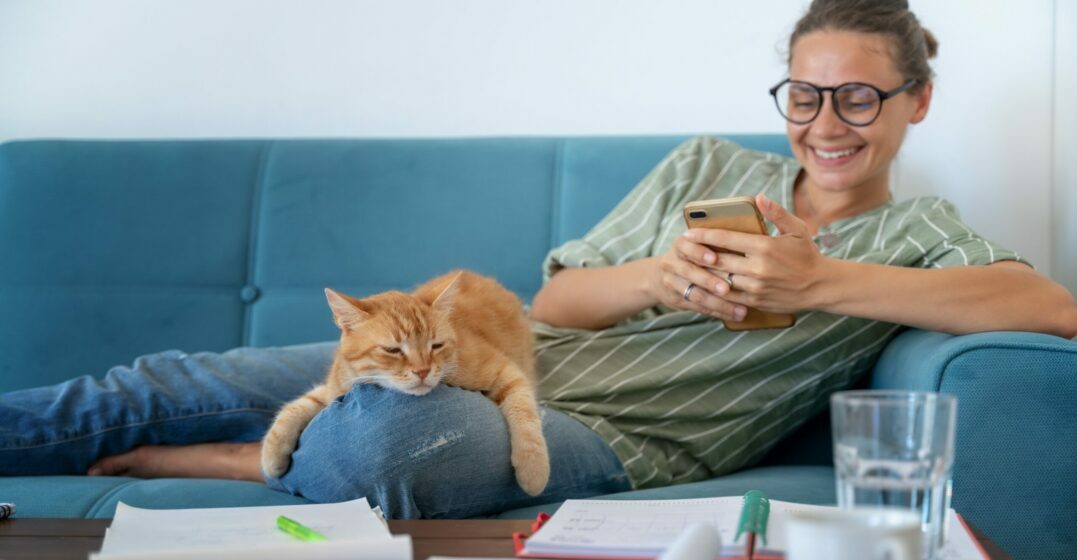 A woman on a couch with a cat studying German nouns for animals