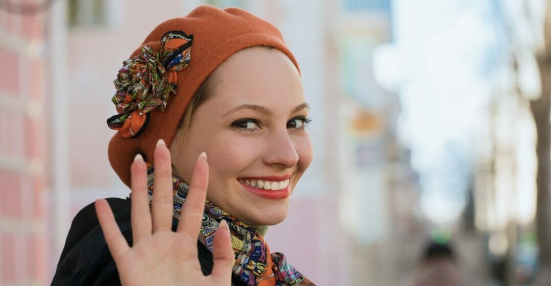 A woman with an orange hat waving goodbye in Spanish