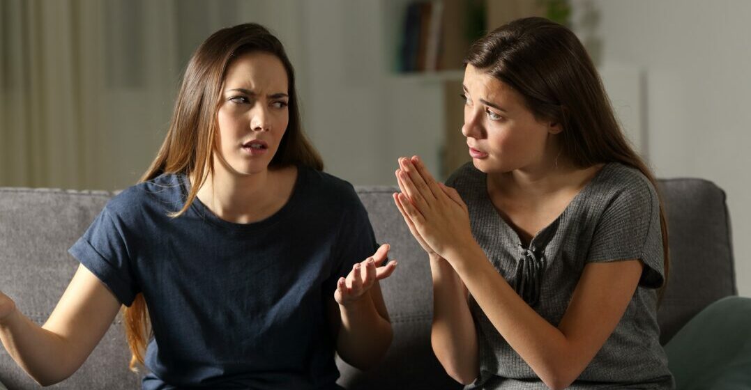 Two women on a couch one is saying sorry in Spanish to the other
