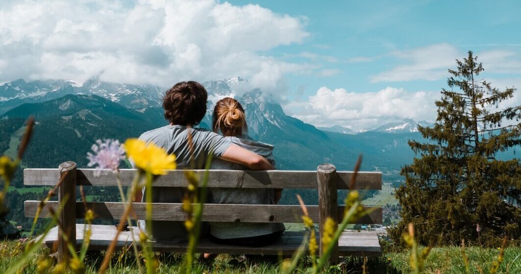 Two peole sitting on a bench in the mountains practising Austrian greetings