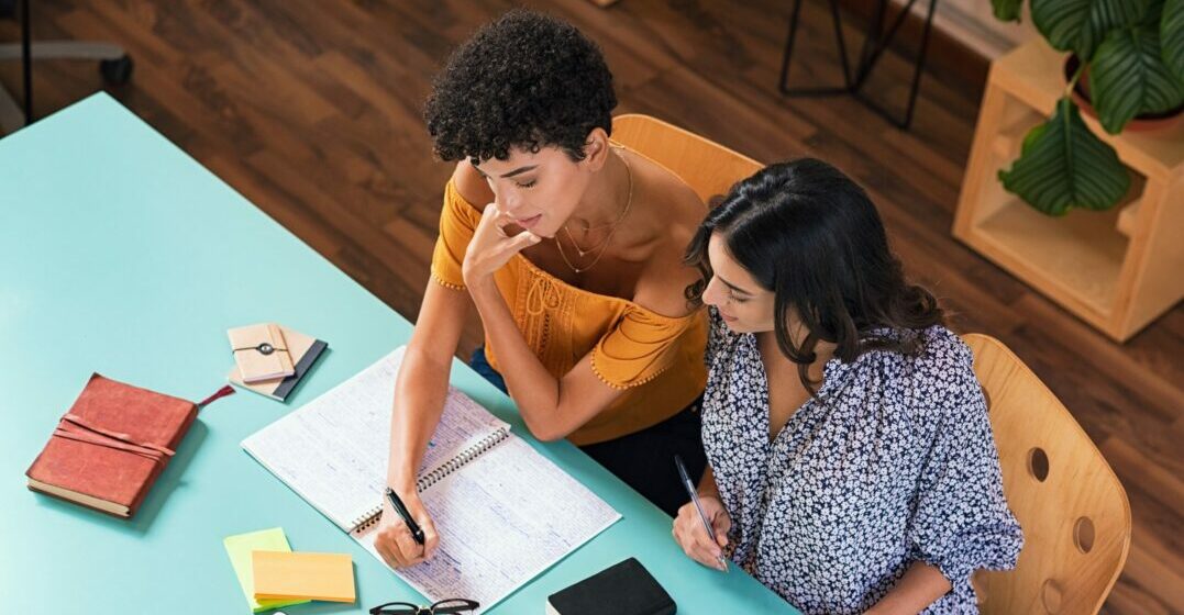 Two young woman at a table studying German adjective decelnsion