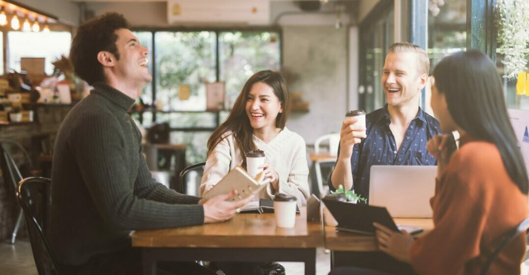 Three friends at a table laughing about hyperbole