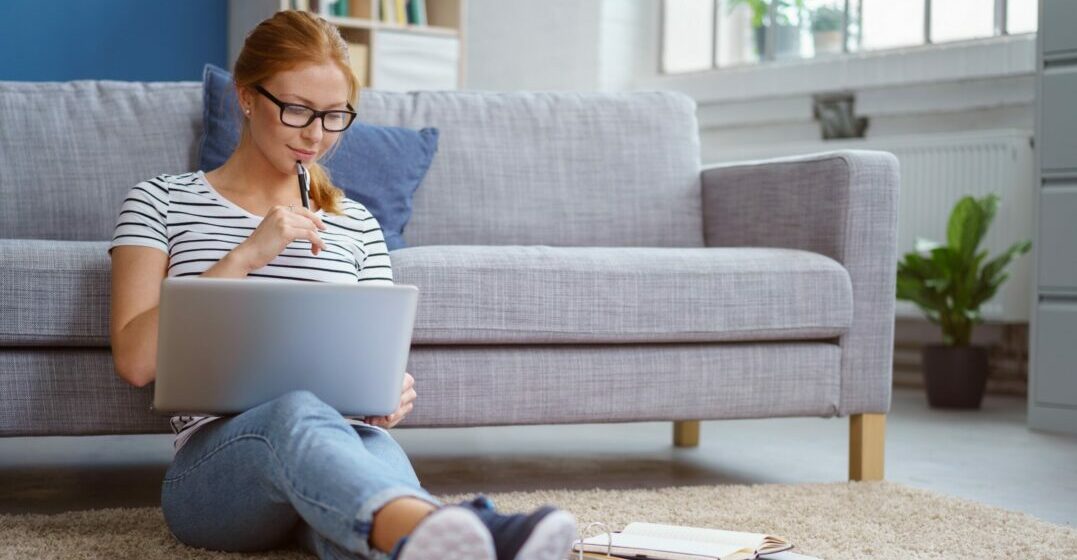A young womand sitting in front of a couch at a laptop studying interrogative pronouns