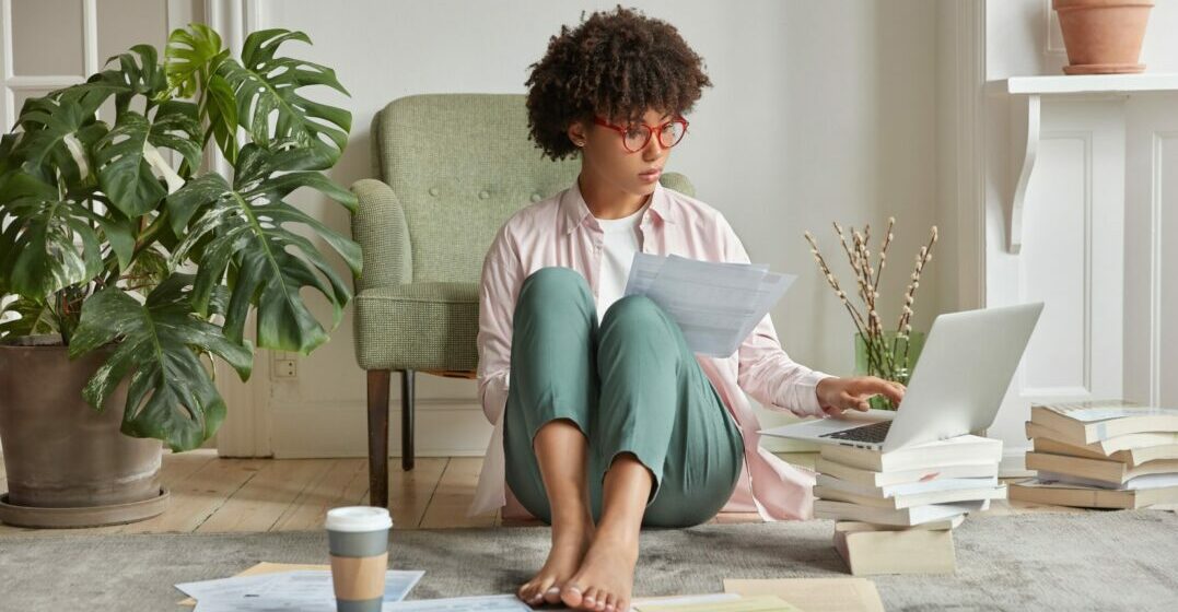 Young woman sitting on the floor with papers aroung her studying linking verbs lists