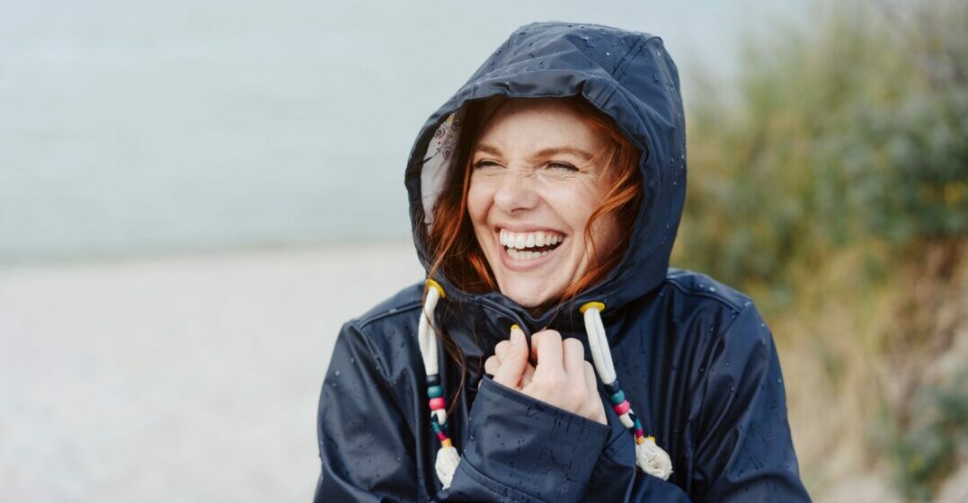 Eine lachende Frau am Strand im Regen redet auf Englisch über das Wetter