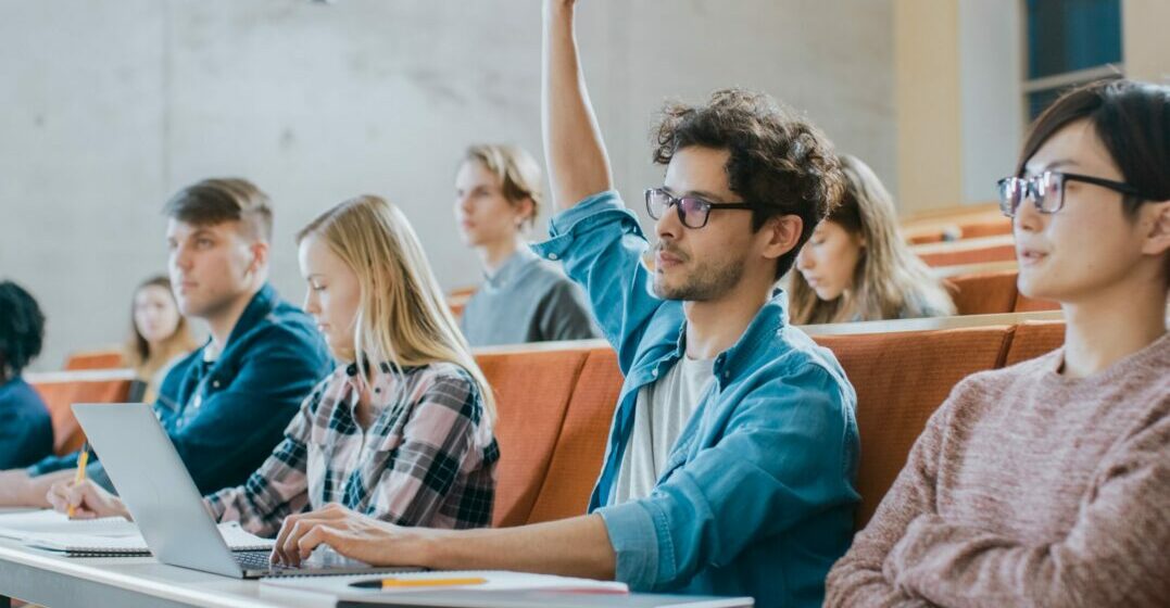 A man in a classroom raising his hand to ask a question in English