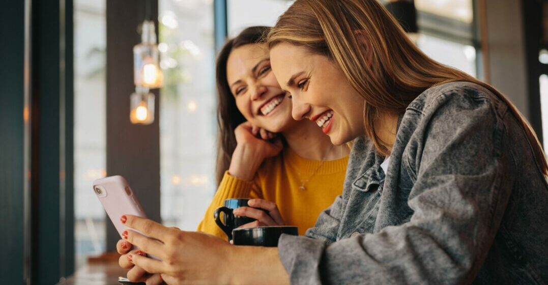 Two women looking at a phone to read funny acronyms and internet slang