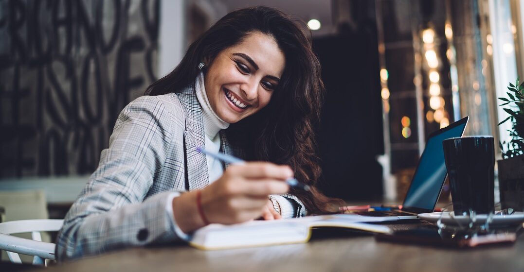 Cheerful woman writing into a notebook what perfect german tense is