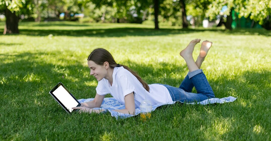 Smiling girl with an e-reader in a park reading