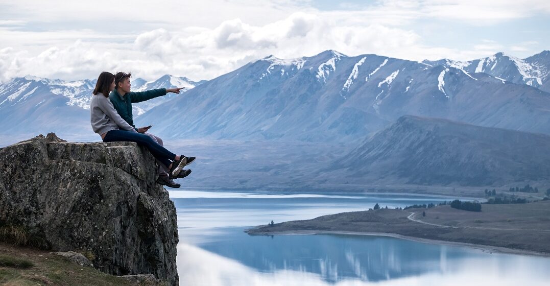 Two people on a rock at a lake in New Zealand speaking slang
