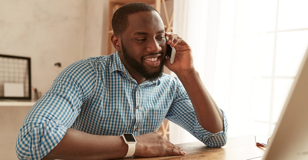 Young man sitting at a laptop talking on the phone in English