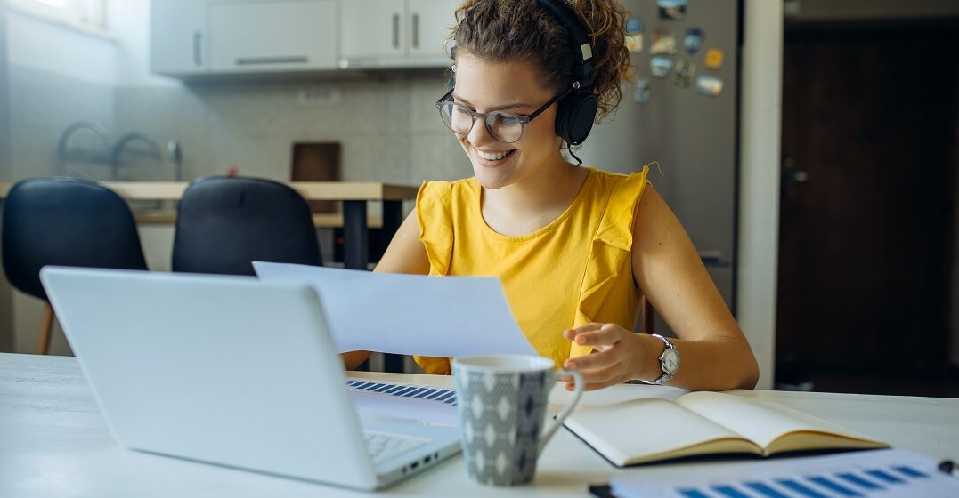 Young woman with headphones at her laptop talking about auxiliary verbs
