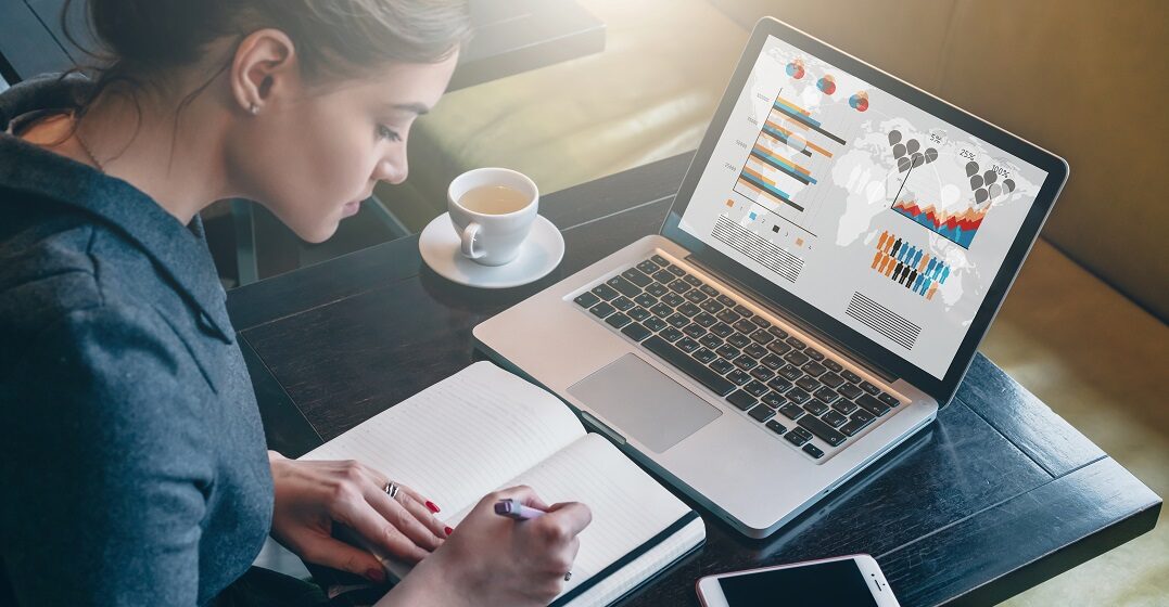 Woman taking notes with a laptop next to her taking into consideration business essy writing tips