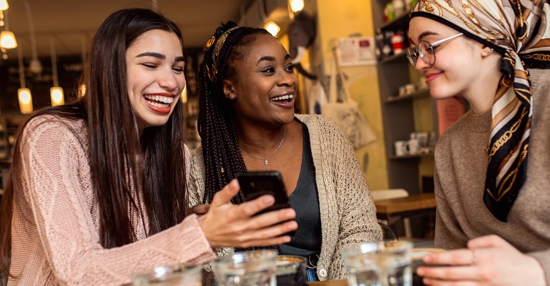 Drei Freundinnen an einem Tisch lachen über englische Zungenbrecher