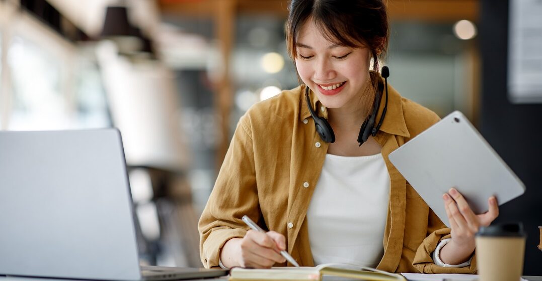 Young Asian woman with her laptop and ad studying the differences between it vs. this