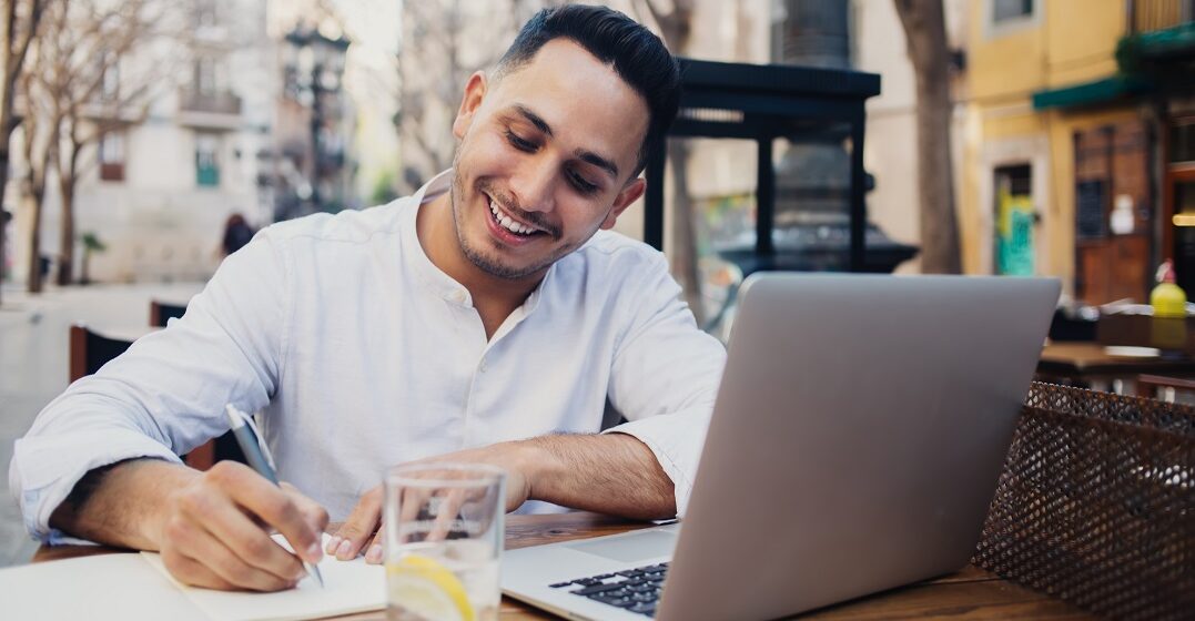 Happy young man sitting outside on his laptop studying the difference between who and whom