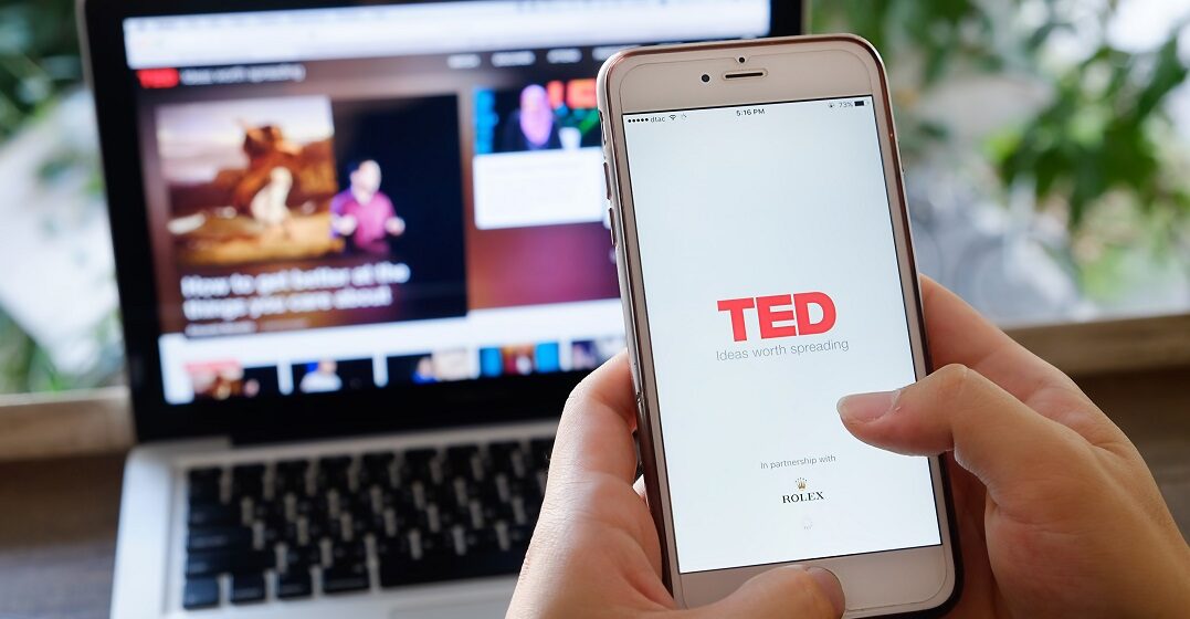 A smartphone with the TED App open and a laptop in the background to watch German TED talks