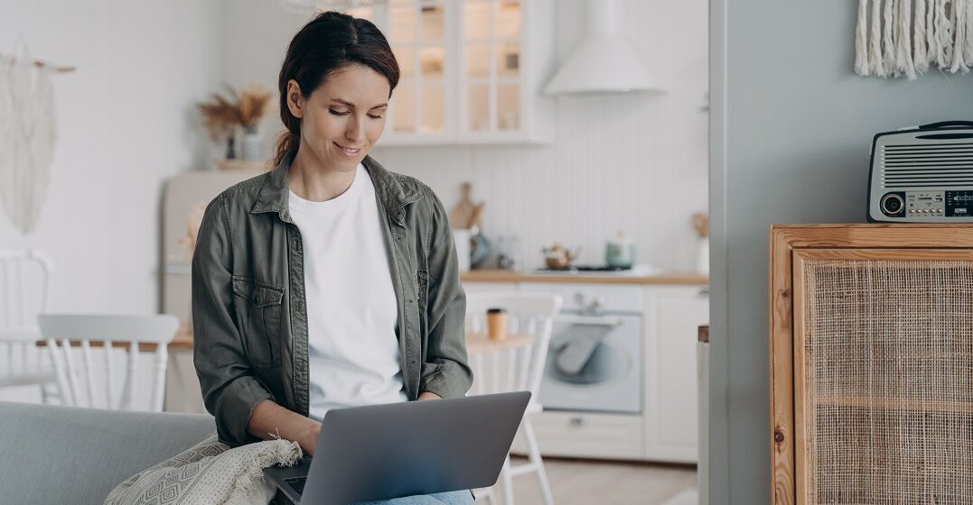 Una mujer sentada en el borde de su sofá con su portátil aprendiendo cómo usar los adjetivos en inglés