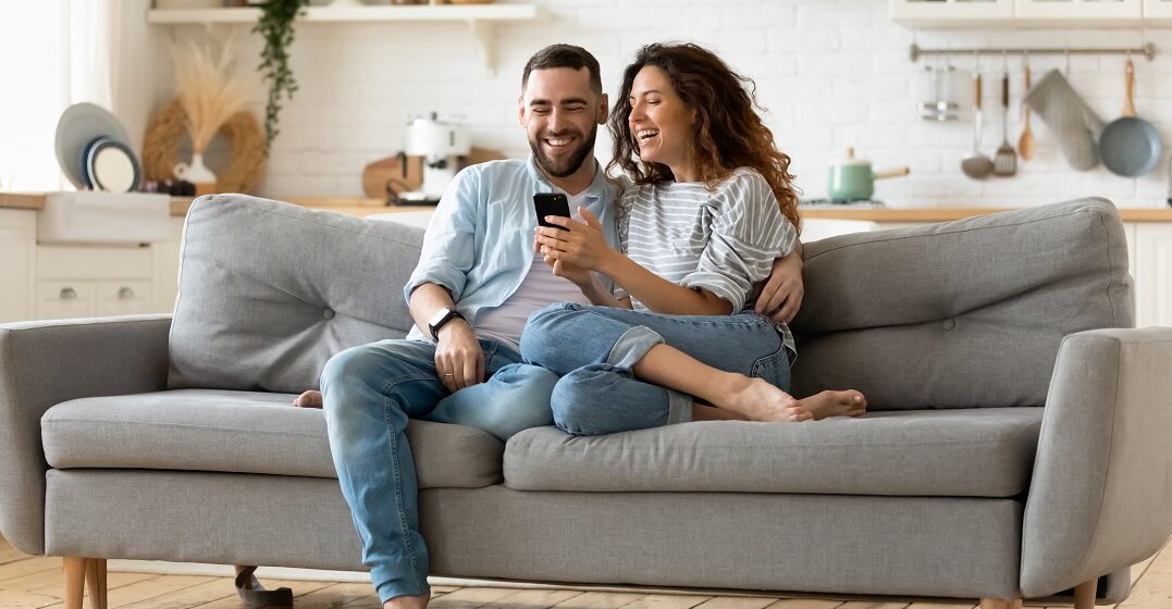 Happy couple who doesn't speak the same language sitting on the couch looking at a phone