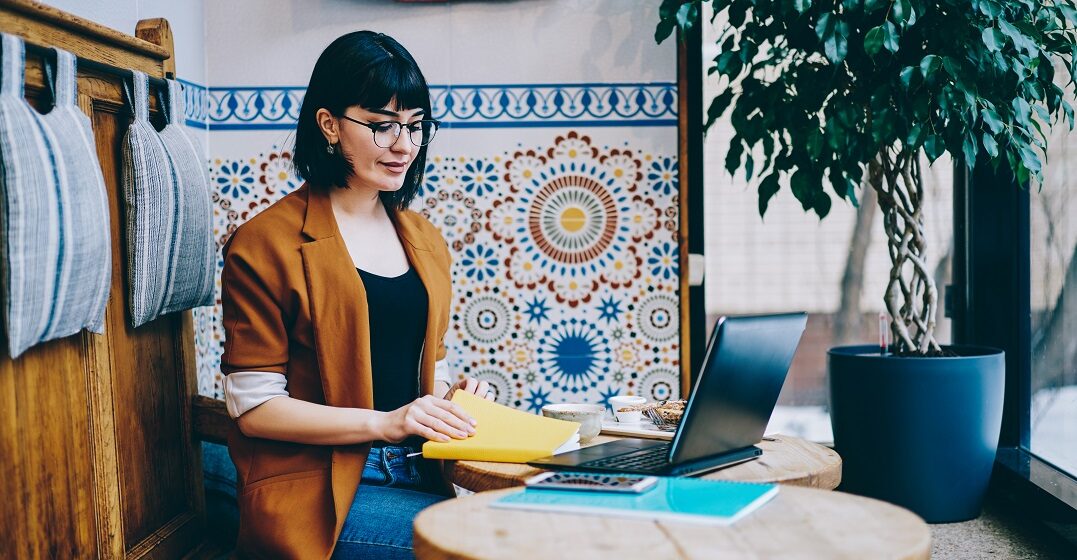 A woman in a colorful café learning the differences between than and then on her laptop