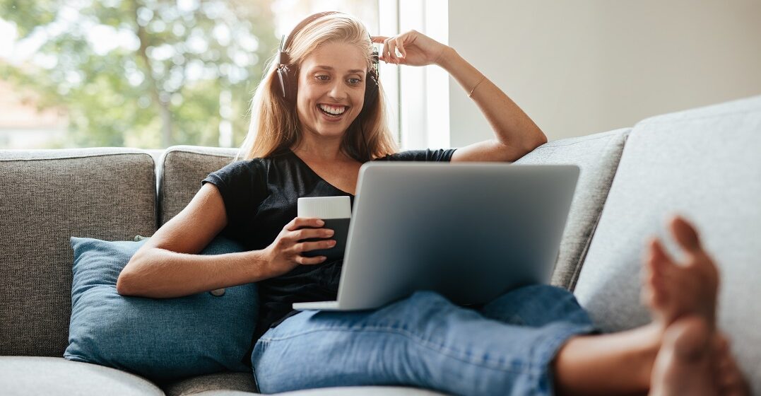 Young woman sitting casually on a couch with a laptop watching cartoons to learn Spanish
