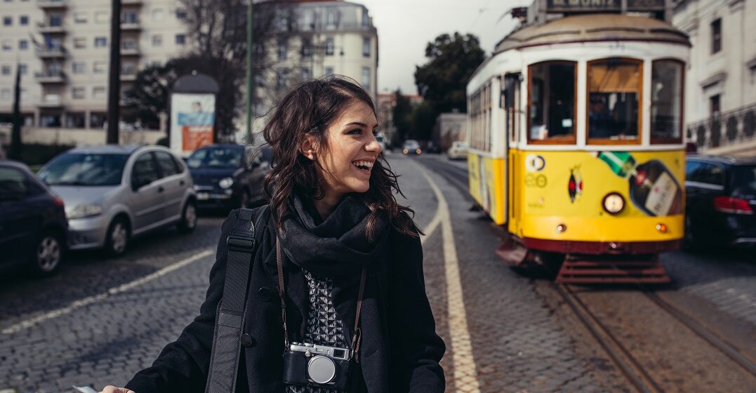 Female traveller next to a Lisbon tram wondering about the cost of living in Europe