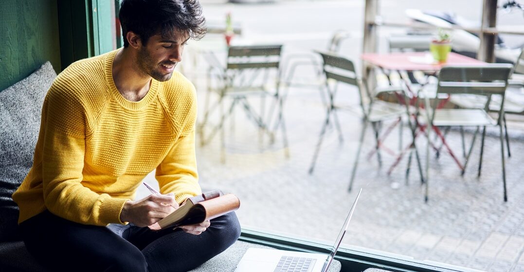 Cheerful man sitting at a cafe taking notes about how hard Spanish is to learn for English speakers