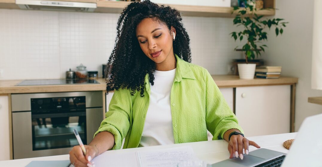 Eine afrikanischstämmige Frau macht Notizen neben ihrem offenen Laptop über Adjective mit Präpositionen im Deutschen